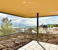 Empty balcony with a panoramic view of a valley and mountains, featuring a glass railing and tiled floor.