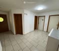 Empty hallway with tiled floor, white walls, multiple wooden doors, and a round ceiling light fixture.