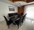 Dining room with a black glass dining table surrounded by six black chairs, a painting on the wall, and a large window with white curtains.