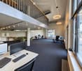 Modern office space with desks, chairs, computers, and a lounge area with green armchairs and a small table.