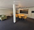 Modern, open-plan room with a green sofa, wooden dining table, yellow chairs, and a compact kitchen area featuring white cabinets, a microwave, and a sink.