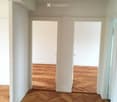 Empty hallway with wooden herringbone flooring and white walls, featuring two open doorways leading to other rooms.