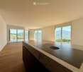 Modern kitchen with a marble countertop, induction cooktop, and large windows offering a scenic mountain view.