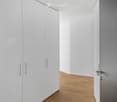 Empty room with white walls, light wooden flooring, and white built-in closet with silver handles.
