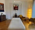 two white couches, two yellow chairs, white wooden floor, wooden table, picture on the wall, wooden cabinet with statue, white curtains, yellow lamp, stack of towels