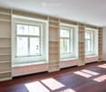 Empty room with built-in shelves and window seats, wooden flooring, and natural light from multiple windows.