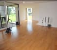 Empty room with wooden flooring, large sliding glass doors leading to a balcony, and a vacuum cleaner placed near the entrance.