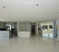 Open-plan, modern space with white walls, polished marble floors, large glass partitions, and recessed lighting. The area includes a kitchen area with cabinets and a countertop, but no furniture or appliances are present.