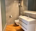 Modern bathroom with a white sink, chrome faucet, large mirror, and a toilet. The walls are textured grey, and the floor is wooden.