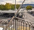 View from a balcony or terrace overlooking a busy urban intersection with pedestrian crossing, traffic, and surrounding greenery.