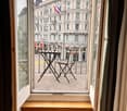 Balcony with a small table and chair, overlooking a street with historic buildings and flags.