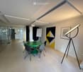 modern office meeting room with glass walls, green table, white chairs, white board, artwork, floor lamp