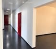 Modern hallway with white walls, black polished floor, and two red doors.