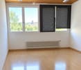 Empty room with wooden flooring, white walls, large windows with blinds, and a radiator.