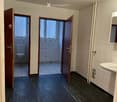 Empty room with dark flooring, white tiled walls, and two open doors leading to bathrooms.
