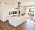 Modern kitchen with white cabinets, a central island, stainless steel appliances, and a view of a balcony with outdoor furniture.