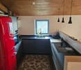 Modern kitchen with wooden ceiling, dark countertops, red refrigerator, sink, stove, and a leafy patterned rug.