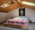 Modern attic bedroom with wooden slanted ceilings, skylights, a bed with a colorful floral duvet, nightstands, a lamp, and a large picture on the wall.