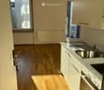 Modern kitchen with light wooden flooring, white cabinets, granite countertop, sink, and oven. Features large windows and a balcony access.