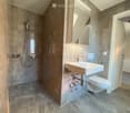 Modern bathroom with grey marble tiles, a white sink, toilet, and a shower area with a glass enclosure.