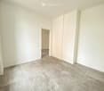 Empty room with light-colored walls, grey tiled floor, and a closed white closet door. No furniture or personal items visible.