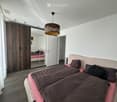 Modern bedroom with a large bed, dark bedding, a wardrobe with mirrored doors, and a hanging lamp with a leopard-print shade.