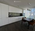 Modern kitchen with white cabinets, dark wooden flooring, a dining table with chairs, and various appliances including a blender, coffee maker, microwave, and oven.