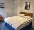 Bedroom with a neatly made double bed, a red wire chair, and two framed pictures on the wall.