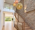Modern hallway with wooden flooring, a staircase with glass railing, stone wall, and decorative pendant lights.
