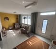 Bright living room with tiled floor, large window, grey armchairs, small table, and decorative items.