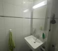 Clean bathroom with white tiled walls, a white sink with a chrome faucet, a mirror with built-in lighting, a towel hanging on the wall, and a soap dispenser on the sink counter.