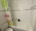 Bathroom with white tiled walls and floor, featuring a toilet, bathtub, and a shower curtain with cartoon characters.