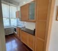 Modern kitchen with wooden cabinets, stainless steel sink, oven, and coffee maker on the counter. Natural light from large windows with blinds.