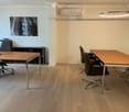 Modern office space with light wood flooring, two office tables, several chairs, a cabinet, and a large circular light fixture.