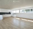 Modern kitchen with white cabinets, a central island, and a sleek black countertop. The space features wooden flooring and large windows allowing natural light to fill the room.