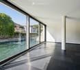 Modern unfurnished room with large floor-to-ceiling windows offering a scenic river view, dark tiled flooring, and white walls.