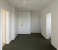 Empty hallway with white walls, dark carpet, and a set of white double doors.