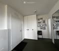 A small, furnished room with white walls, a large white wardrobe, two chairs with leopard print cushions, and several framed pictures on the wall.