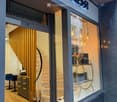 Modern storefront with glass display window, interior visible with modern furniture, lighting, and decorative items. The entrance features a staircase leading up to the shop.