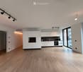 Modern, minimalist kitchen with white cabinets, wooden flooring, and large windows. Features include an oven, microwave, and sink.