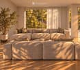 Bright living room with large windows and sliding glass doors leading to a balcony, featuring a sectional sofa, coffee table, and potted plants.