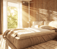 Modern bedroom with a large bed, nightstand, table lamp, and books. Natural light streams in through a window with sheer curtains, complemented by warm wooden paneling and a patterned rug.