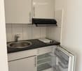 Compact kitchen with white cabinets, stainless steel sink, range hood, and open refrigerator.