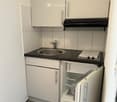 Compact kitchen with white cabinets, black countertop, stainless steel sink, and small refrigerator.