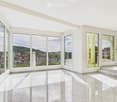 Bright, empty room with large windows and a marble floor, offering a scenic view of the city and surrounding landscape.