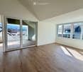 Empty room with wooden flooring, large windows, and a sliding glass door leading to a balcony.