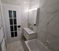 Modern bathroom with marble tiles, a white sink, bathtub, and a large mirror with built-in lighting. Features a frosted glass window and a white radiator.