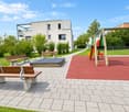 Outdoor area with benches, playground equipment, and a modern building in the background.