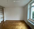 Empty room with wooden flooring, white walls, a window with a view, a radiator, and built-in wooden shelves.