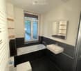 Modern bathroom with black tiles, white fixtures, a bathtub, sink, toilet, mirror, and built-in shelves.